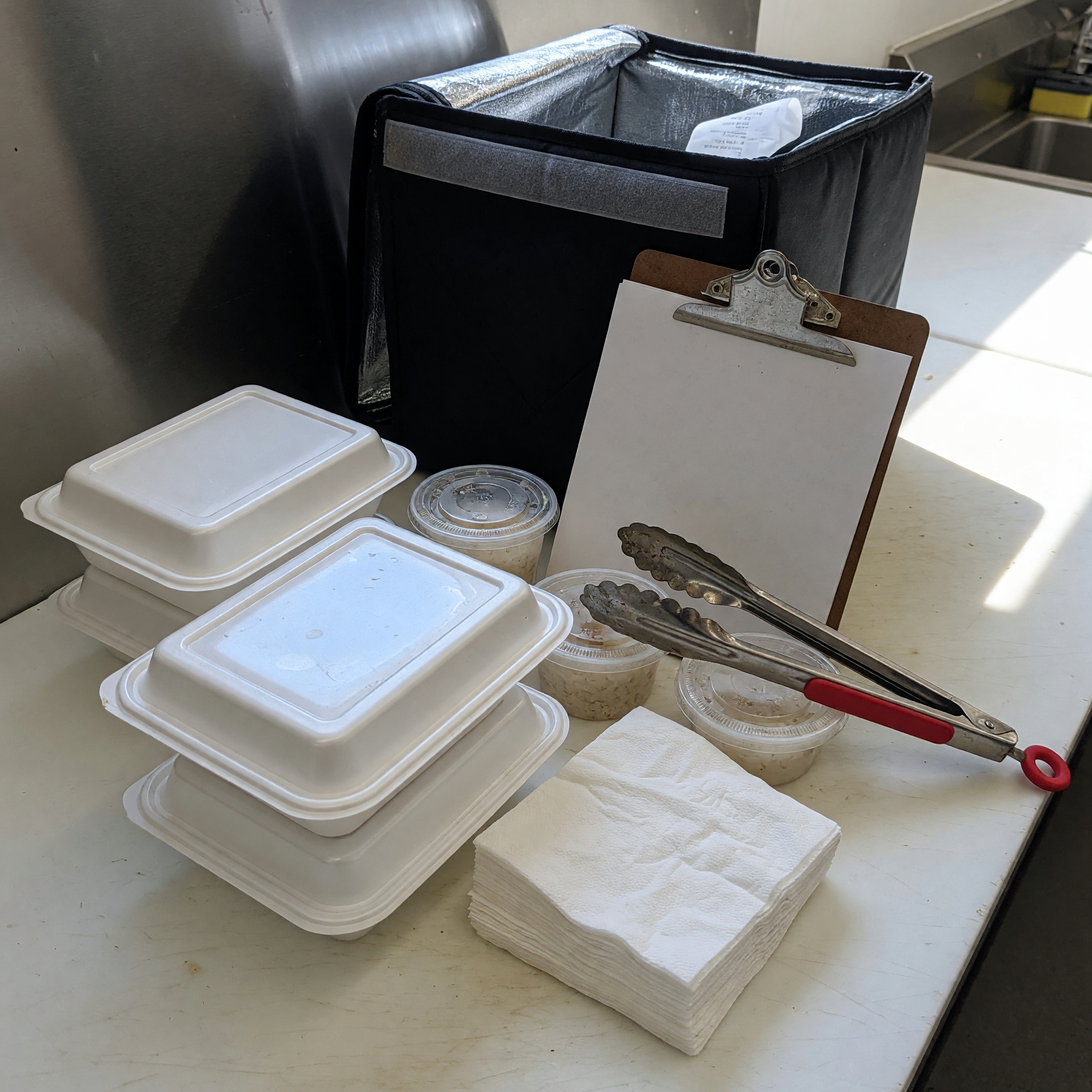 Contenedores de catering, pinzas, servilletas y bolsa termica listos para una entrega local