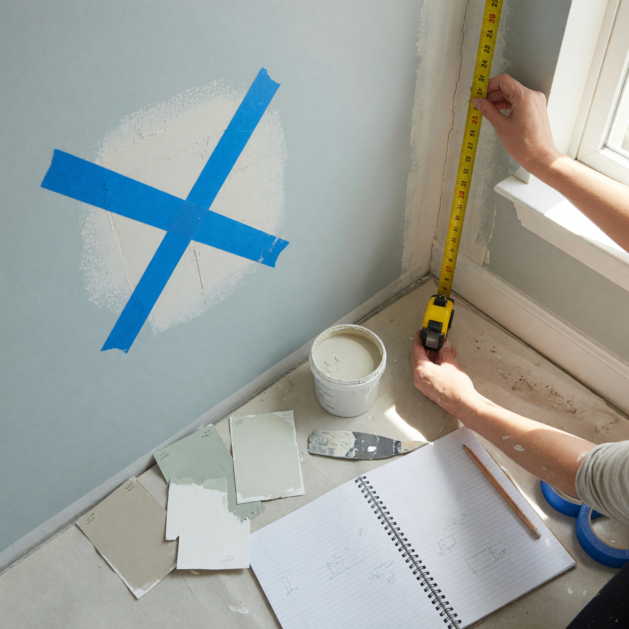 Pintor revisando una esquina de pared con cinta, muestras de color y herramientas de preparación