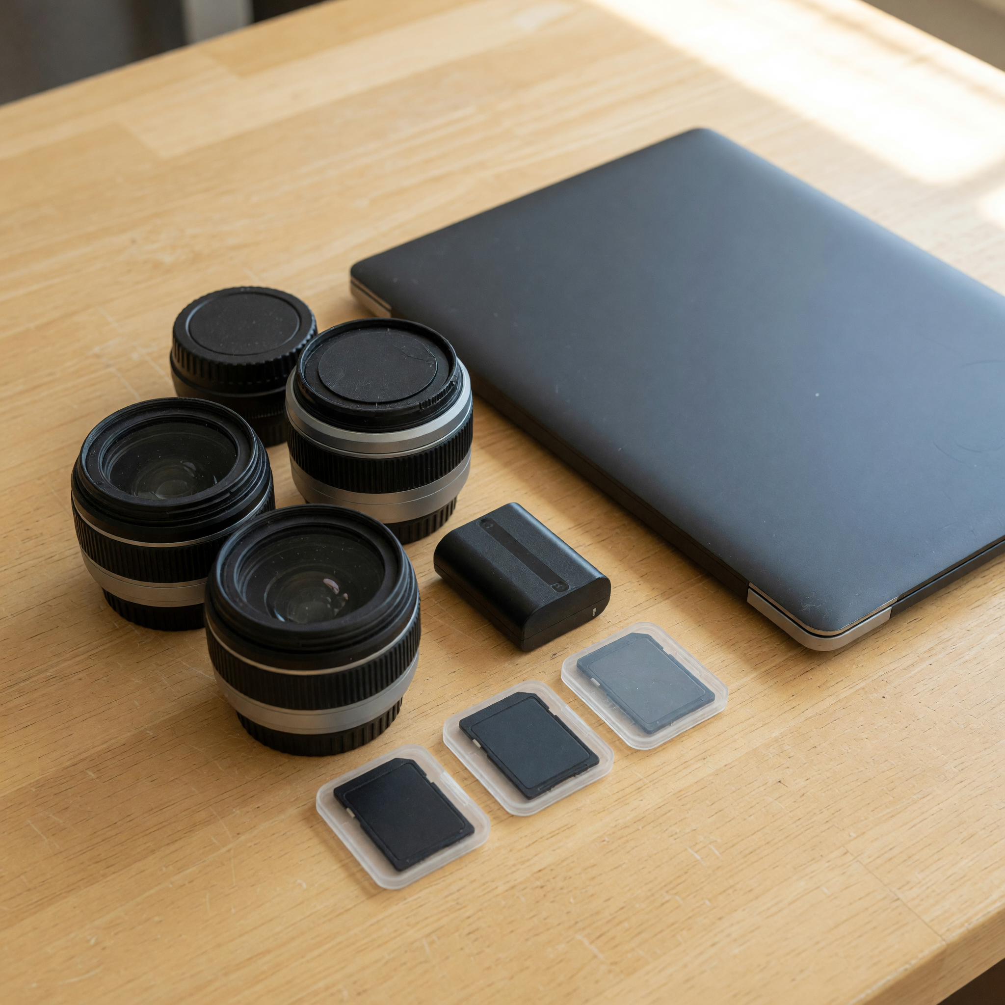 Camera lenses, blank memory cards, battery, and closed laptop prepared for an event photography job
