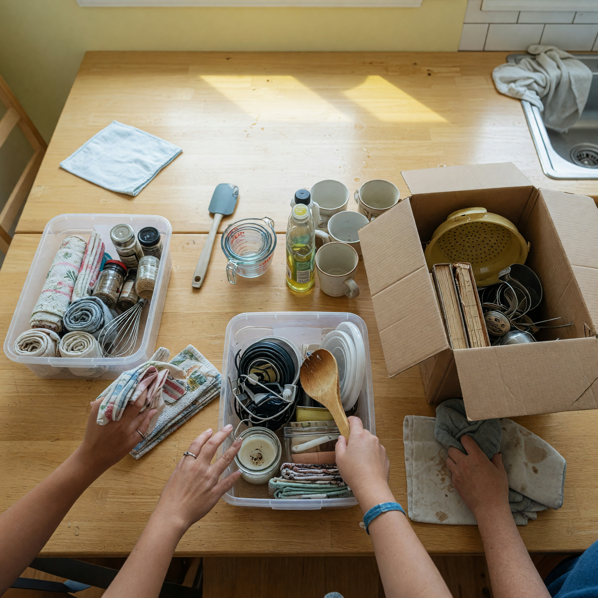 Hands sorting household items into clear bins and donation boxes for a home organization service listing