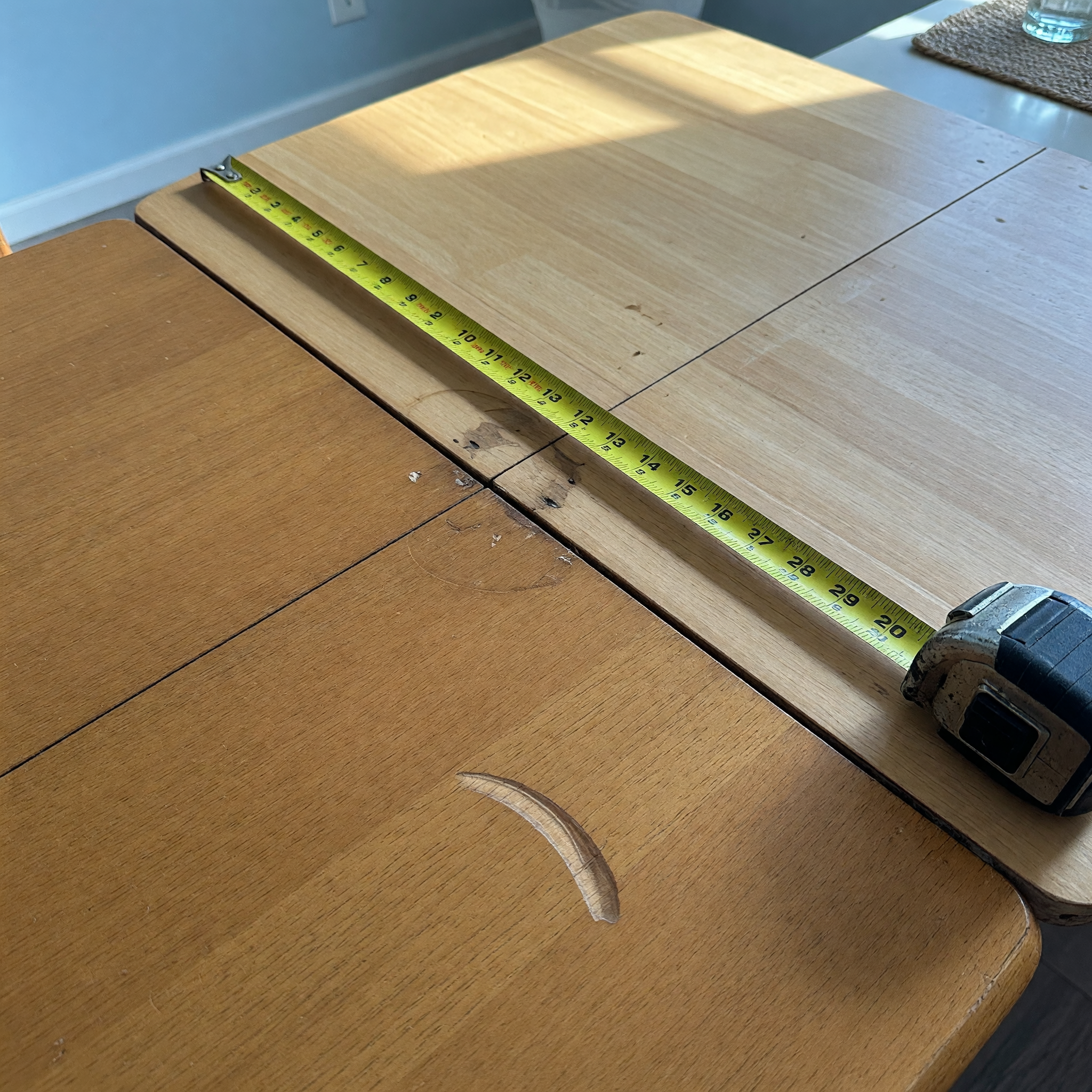 Close detail of a dining table leaf seam with a tape measure across the tabletop for a used furniture listing