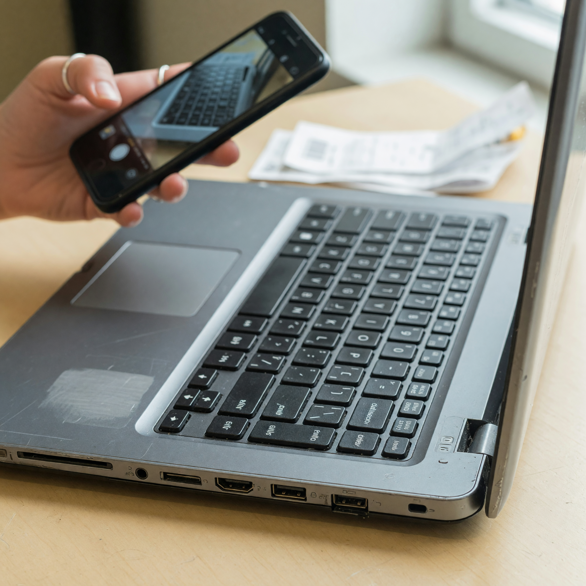 Close view of a used laptop's side ports while a hand photographs the keyboard for a listing