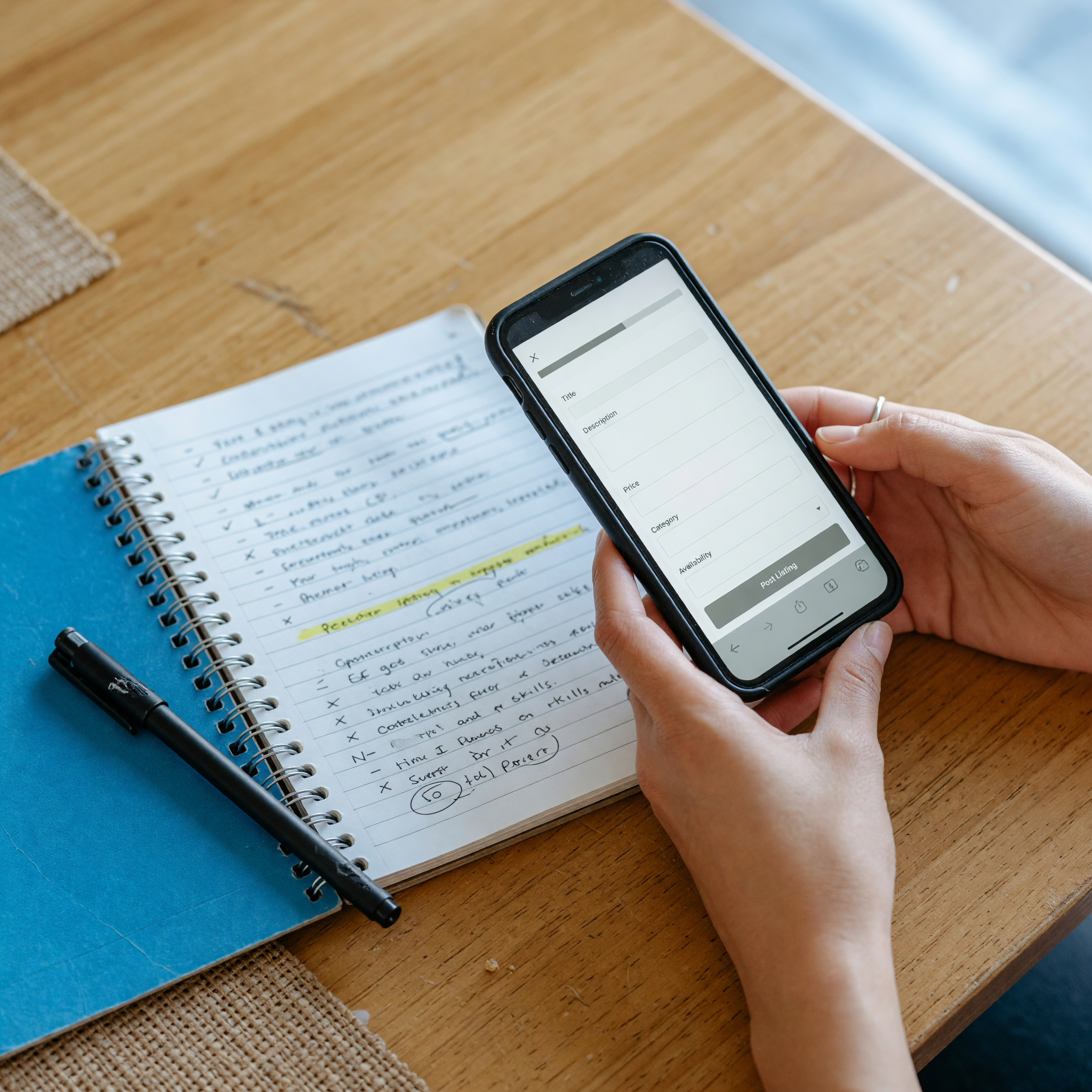 Hands holding a phone with a blank listing form next to a notebook listing skills, availability, and hourly rate