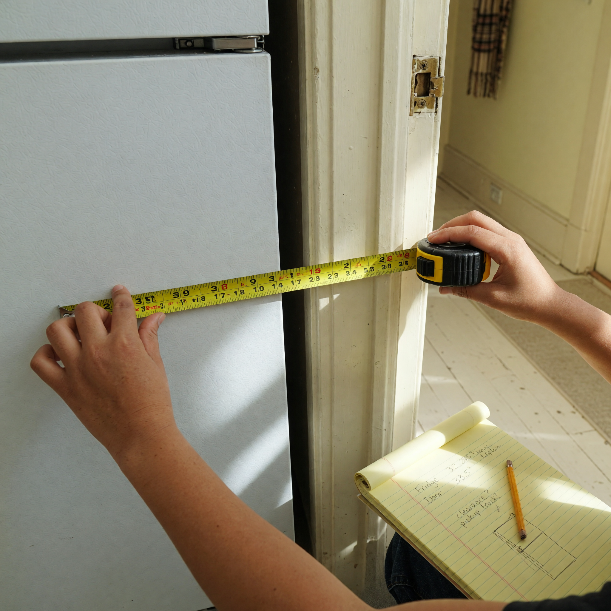 Hands holding a tape measure against a refrigerator next to a doorway to check pickup fit